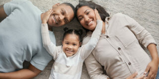 Portrait of a mixed race family of three relaxing on the lounge floor at home. Loving black family being affectionate on a carpet. Young couple bonding with their daughter at home.